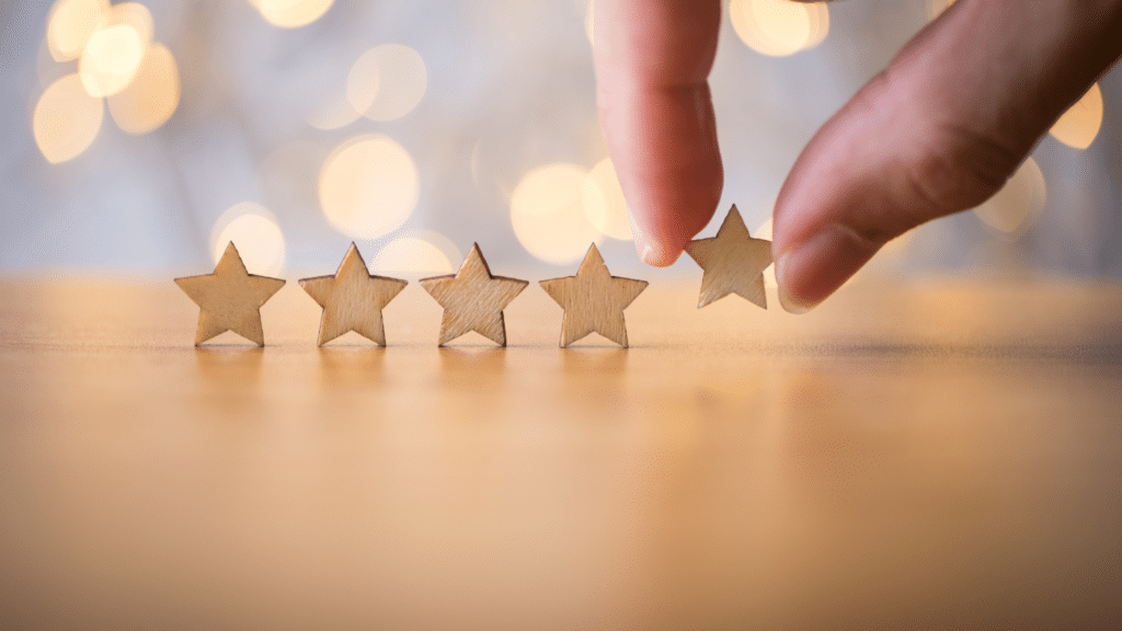 four small wooden stars on a table in front of lights. Two fingers are placing the fifth star on the table. Church Equip Curriculum